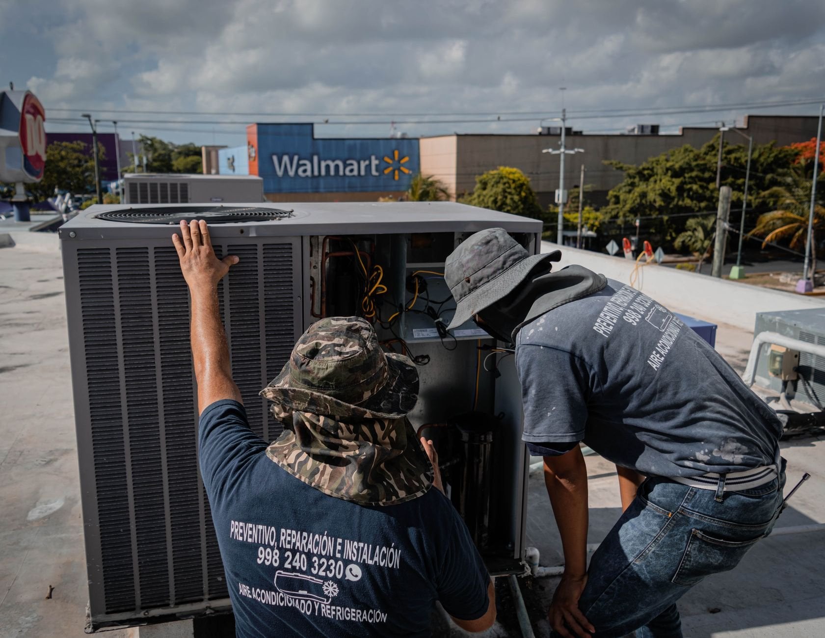 Two technicians repair a rooftop HVAC unit, demonstrating skilled trades work.